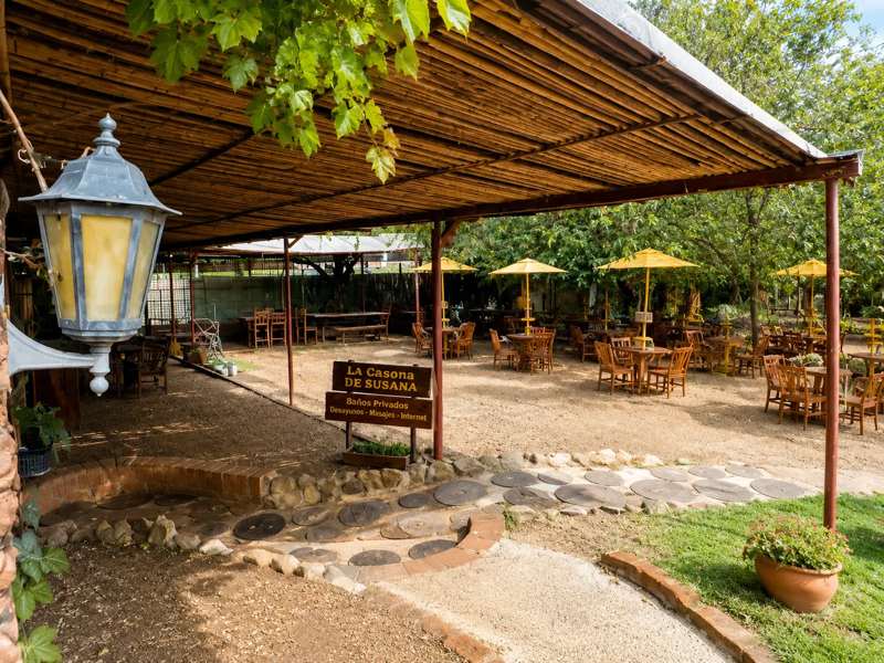 Sector de comedor al aire libre con mesas de madera, sombrillas amarillas y el cartel de La Casona de Susana