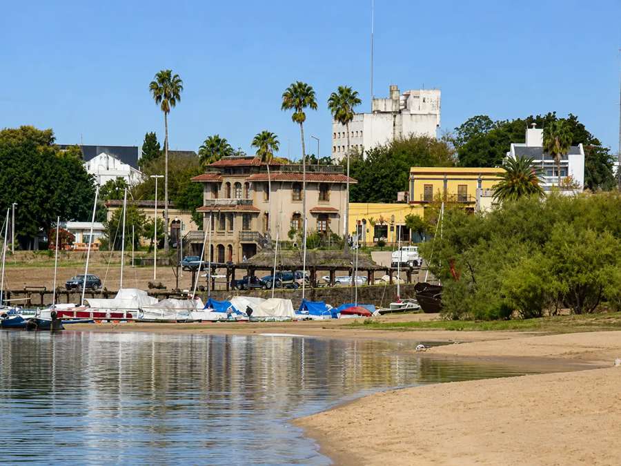 Costanera de Colón con veleros, playa de arena y edificios históricos entre las palmeras