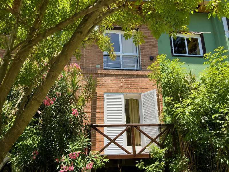 Ala de habitaciones de ladrillo con balcón de madera entre árboles y plantas florecidas